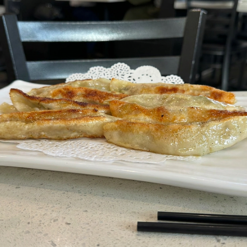 Golden-brown pan-fried dumplings arranged on a white rectangular plate in a restaurant dining area.